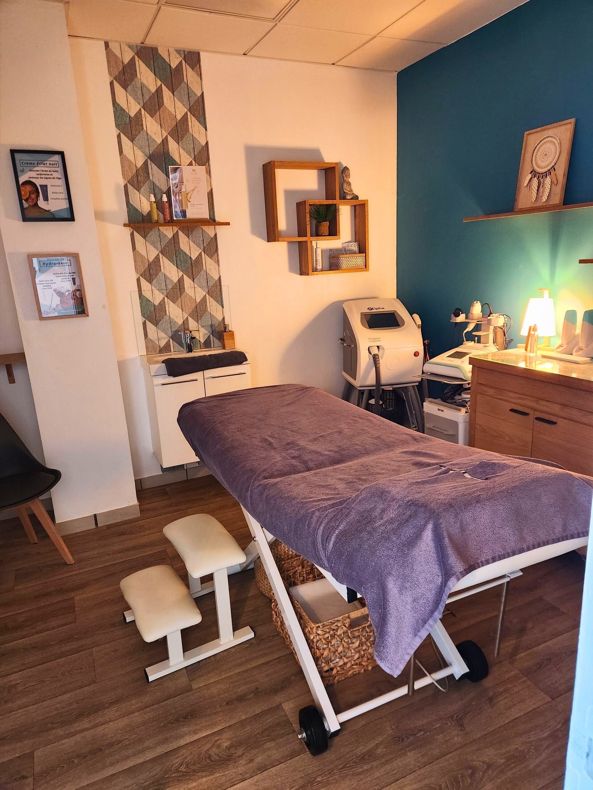 Salle de massage avec table violette, petits tabourets blancs, étagères avec produits et mur d'accent turquoise.