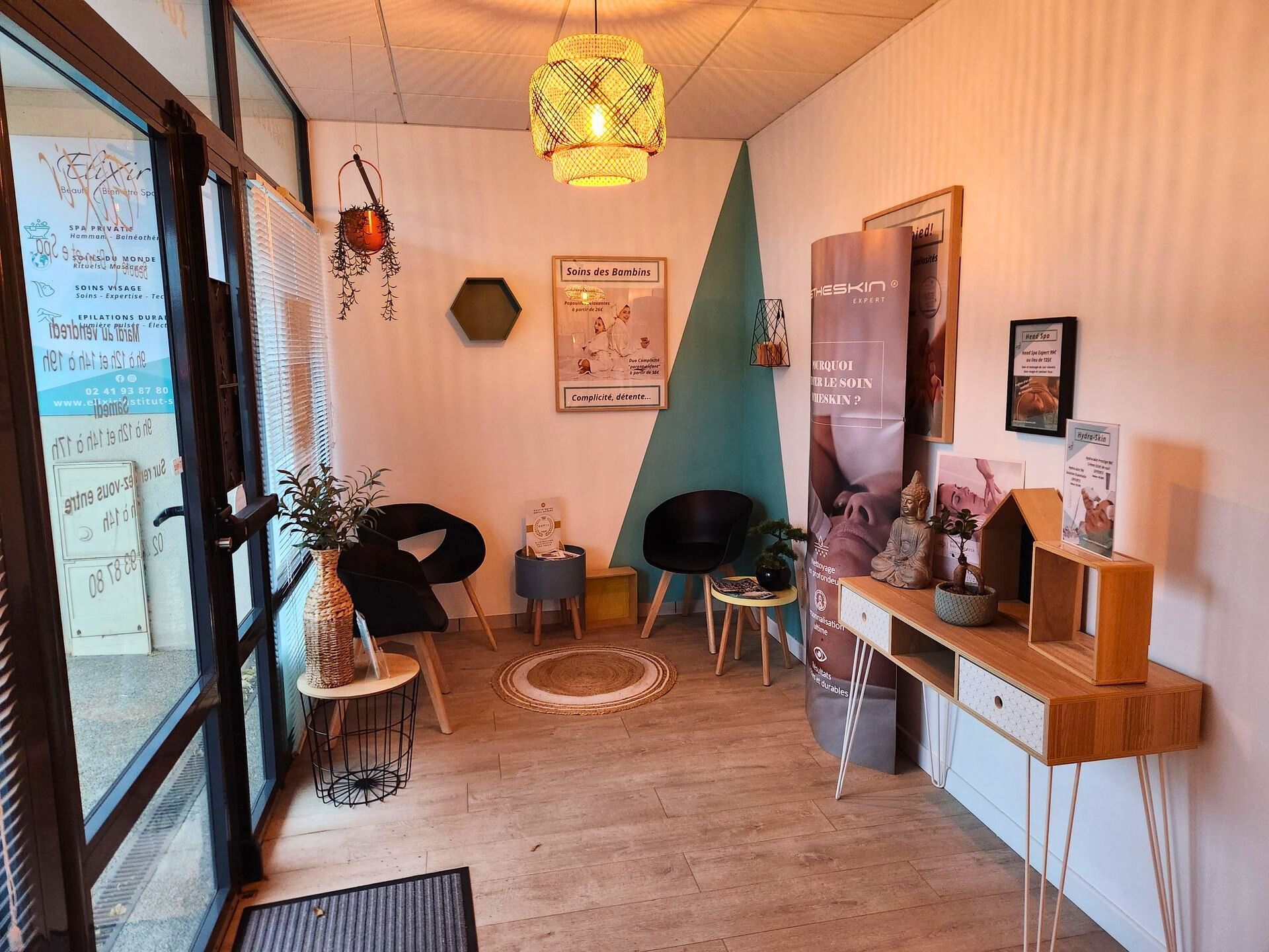 Salle d'attente confortable avec chaises noires, guéridons en bois et bureau. Mur d'accent turquoise, plantes suspendues et lumière naturelle.