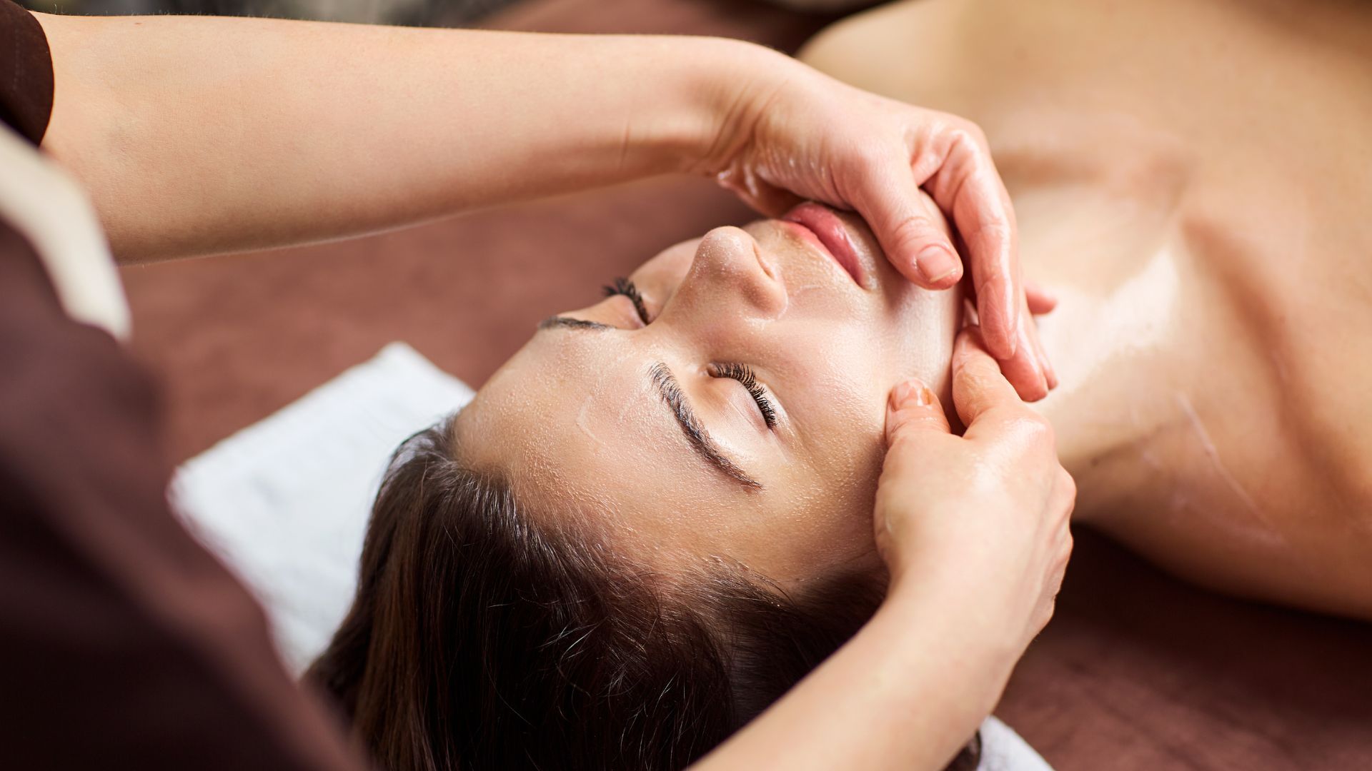 Des mains massent le visage d'une personne. Celle-ci est allongée, les yeux fermés.