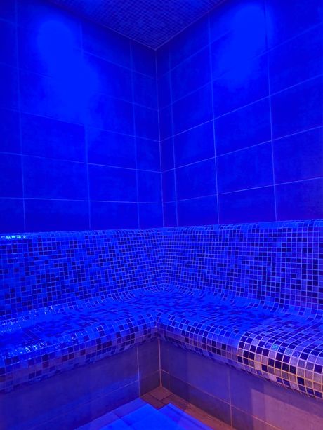 Hammam éclairé en bleu avec murs carrelés et banquettes intégrées.