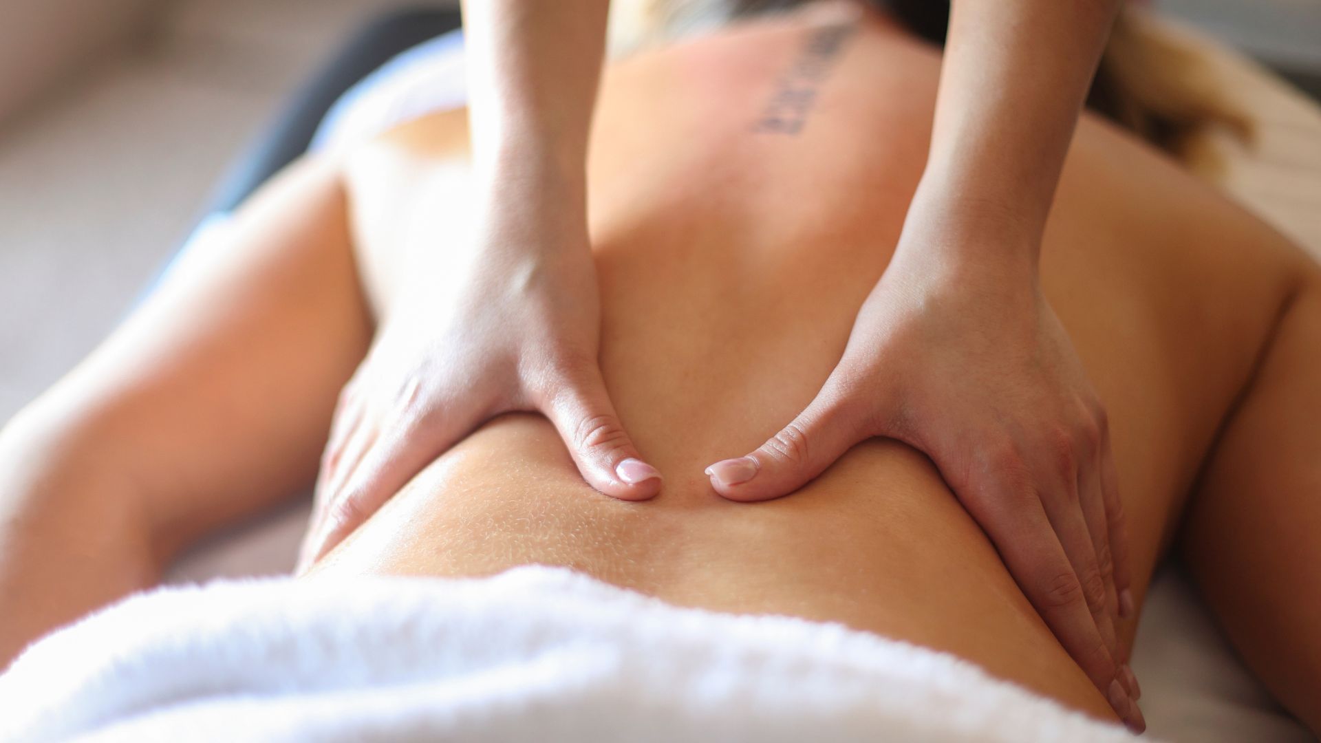 Des mains massent le dos d'une personne, probablement à des fins thérapeutiques.