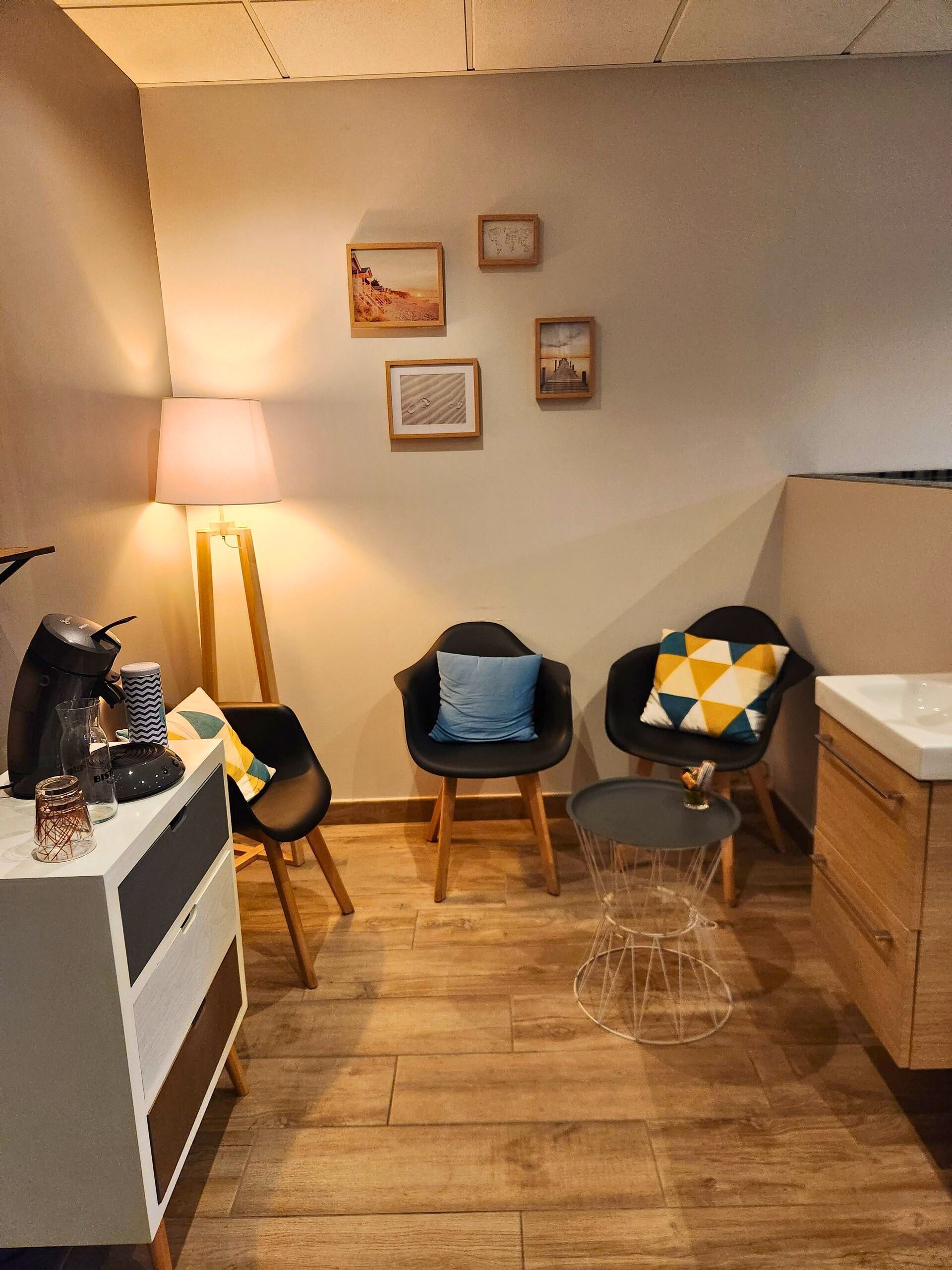 Espace d'attente confortable avec chaises, petite table, œuvres d'art, lampadaire et coin café.