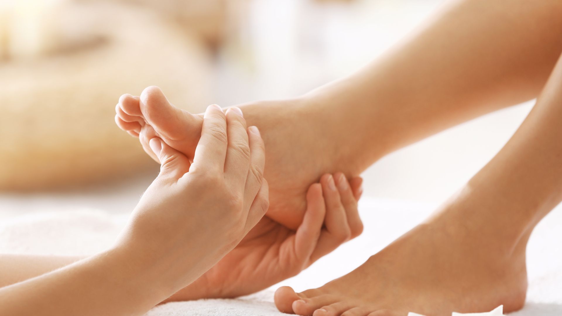 Des mains massent un pied sur une serviette blanche.
