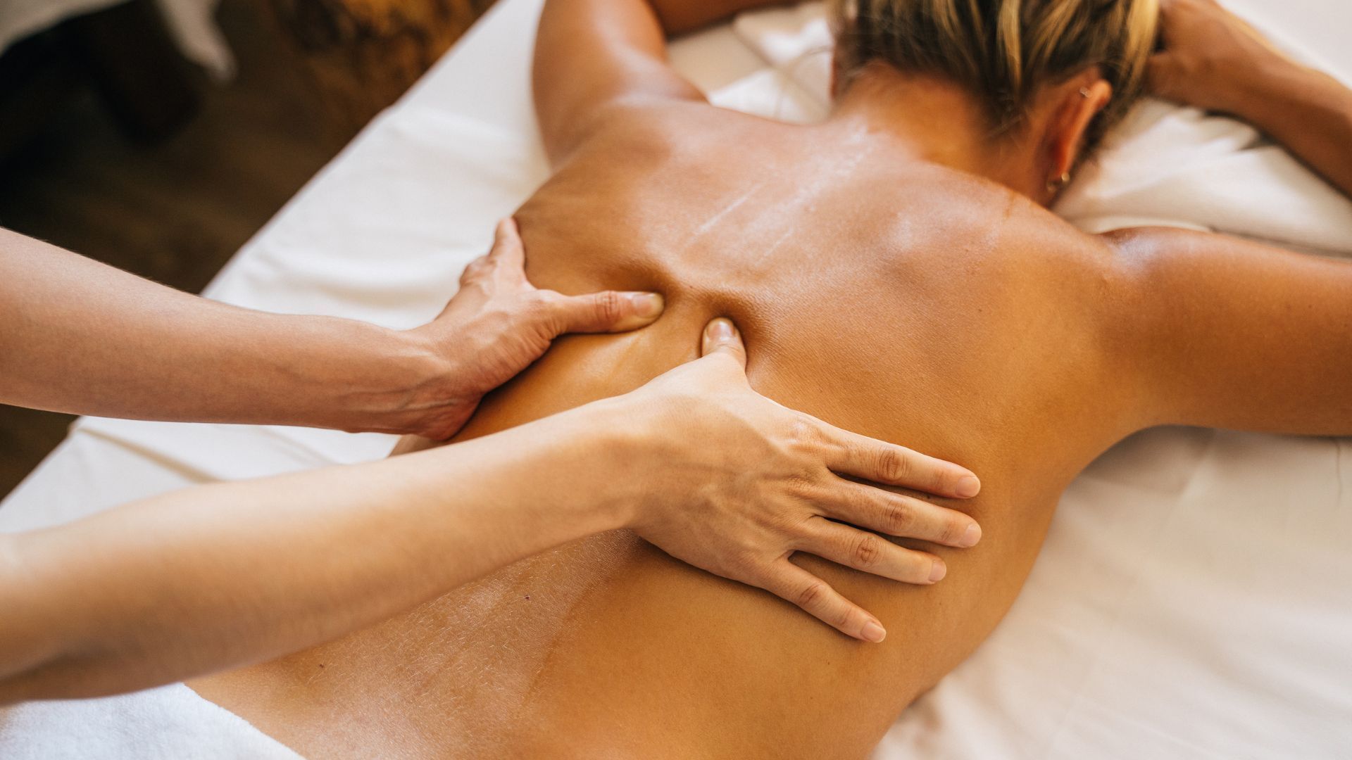 Une personne reçoit un massage du dos sur une table de massage blanche. Les mains pétrissent son dos.