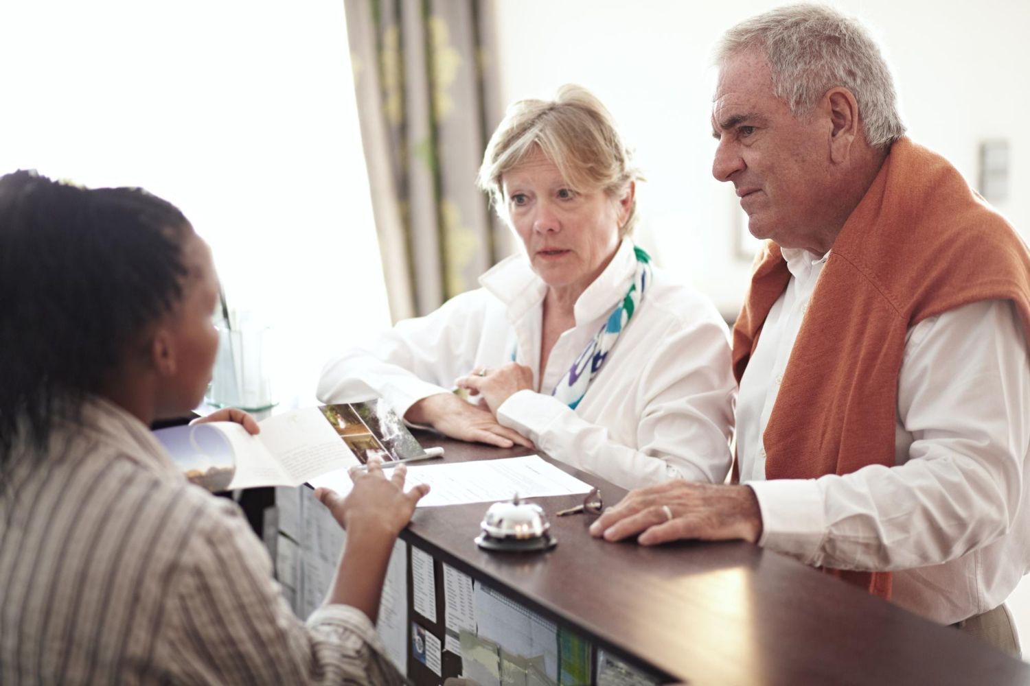 A receptionist discusses documents with a couple at a hotel front desk.