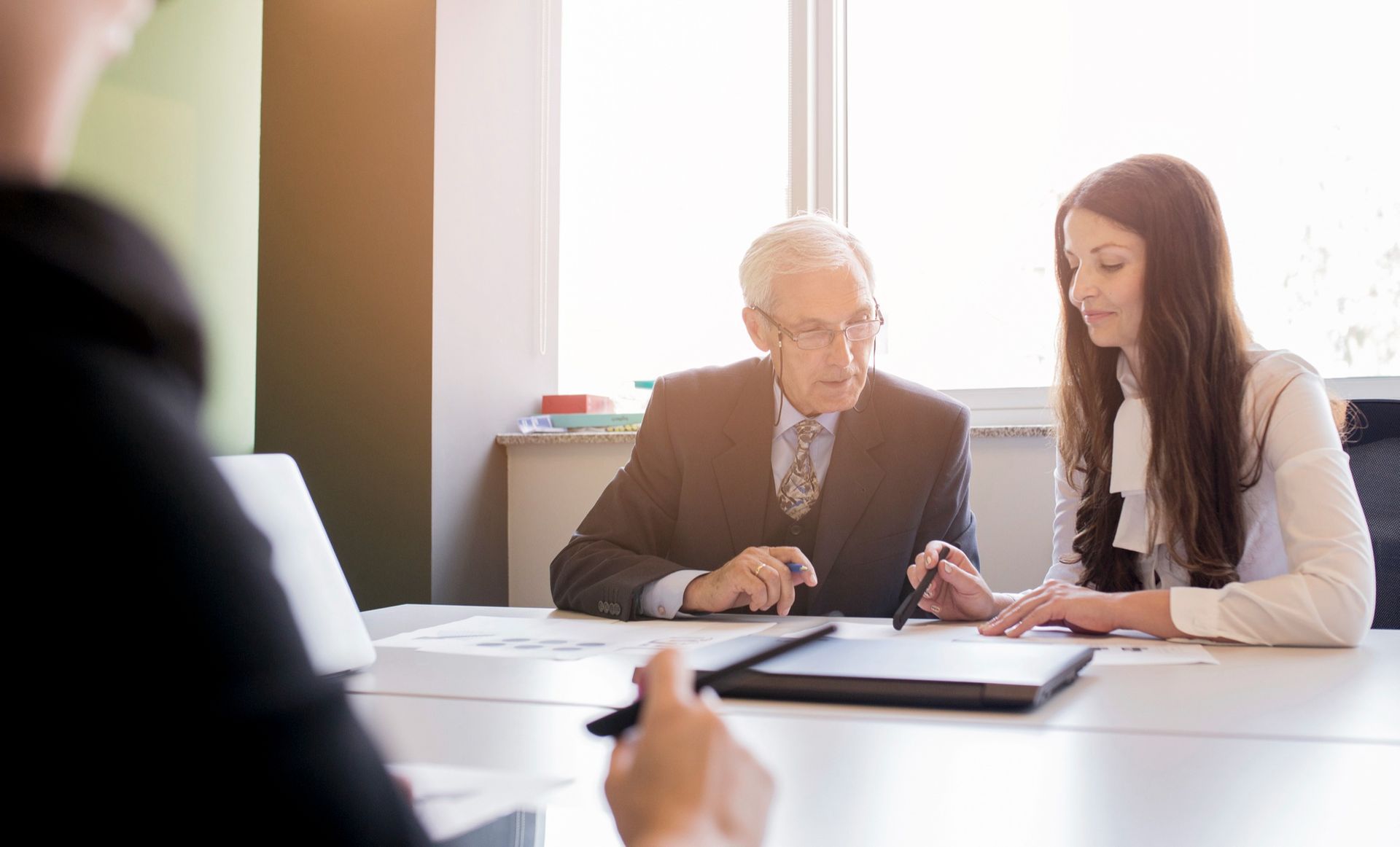 Two professionals in business attire collaborate while reviewing documents on a desk in a bright office.