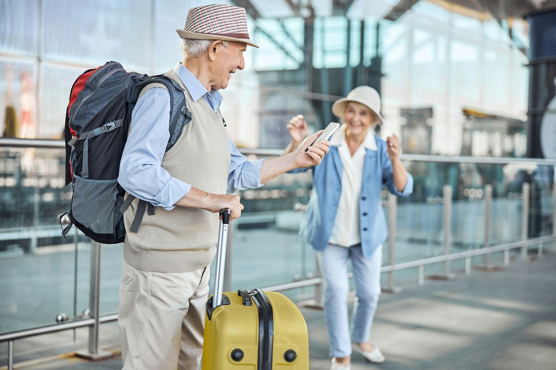 Two travelers with luggage and backpacks standing in a modern airport terminal.