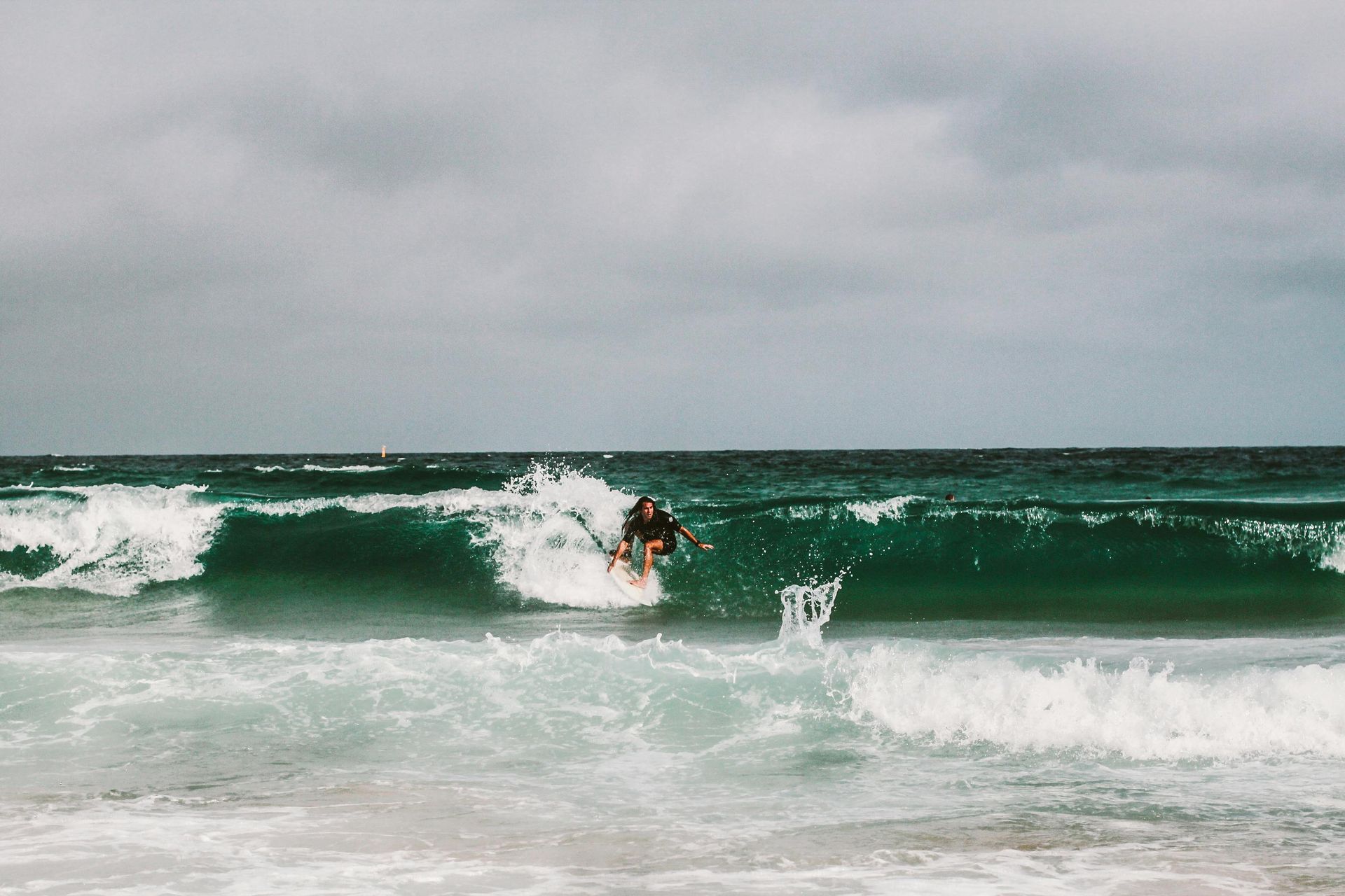 A person surfing on a turquoise wave under a cloudy, overcast sky.