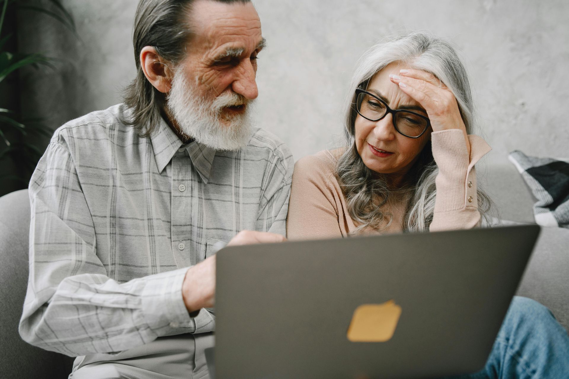 Two people sitting on a couch, looking at a laptop with focused and concerned expressions.