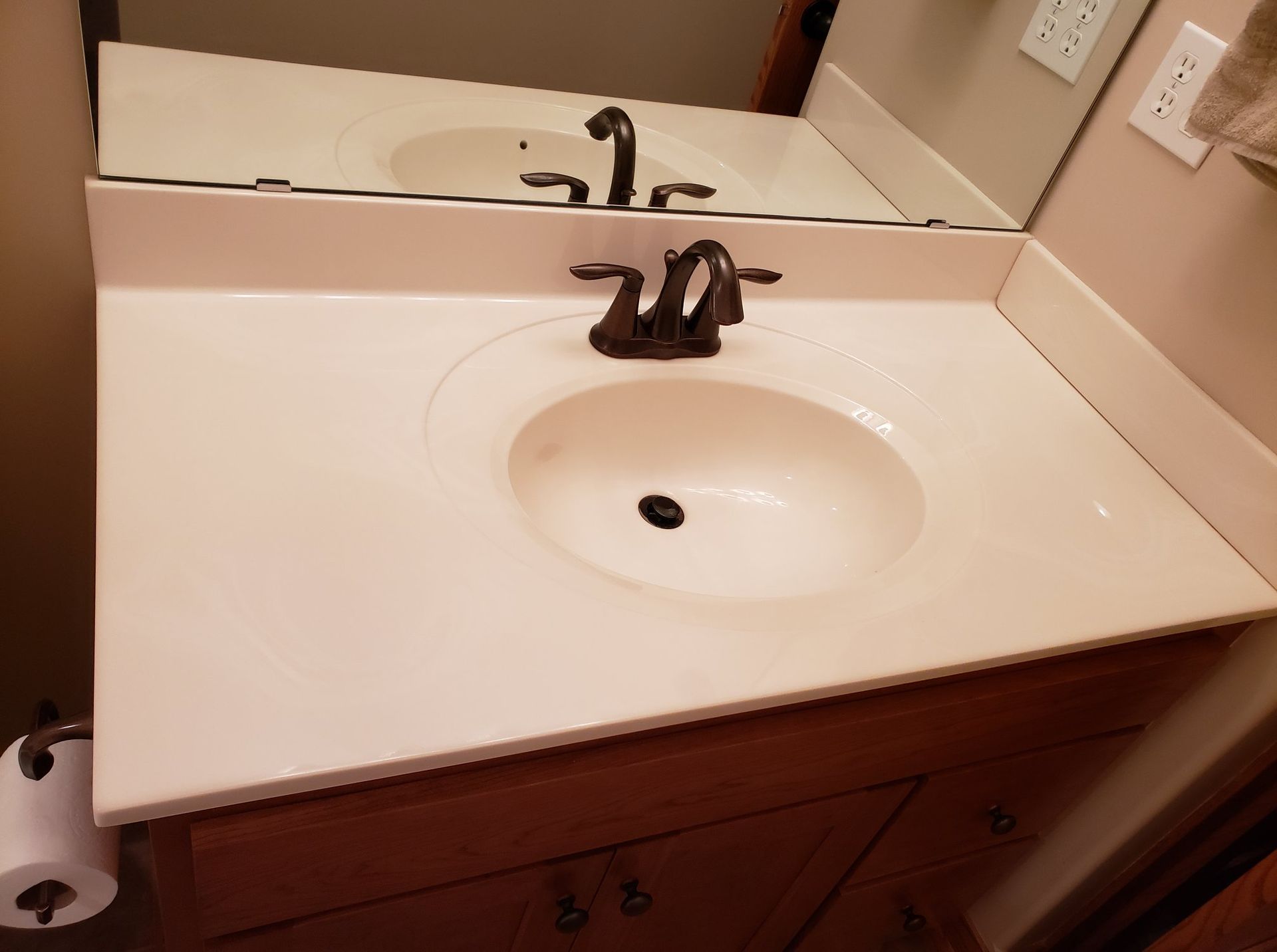 Bathroom sink with a white countertop, brown faucet, and brown cabinet.