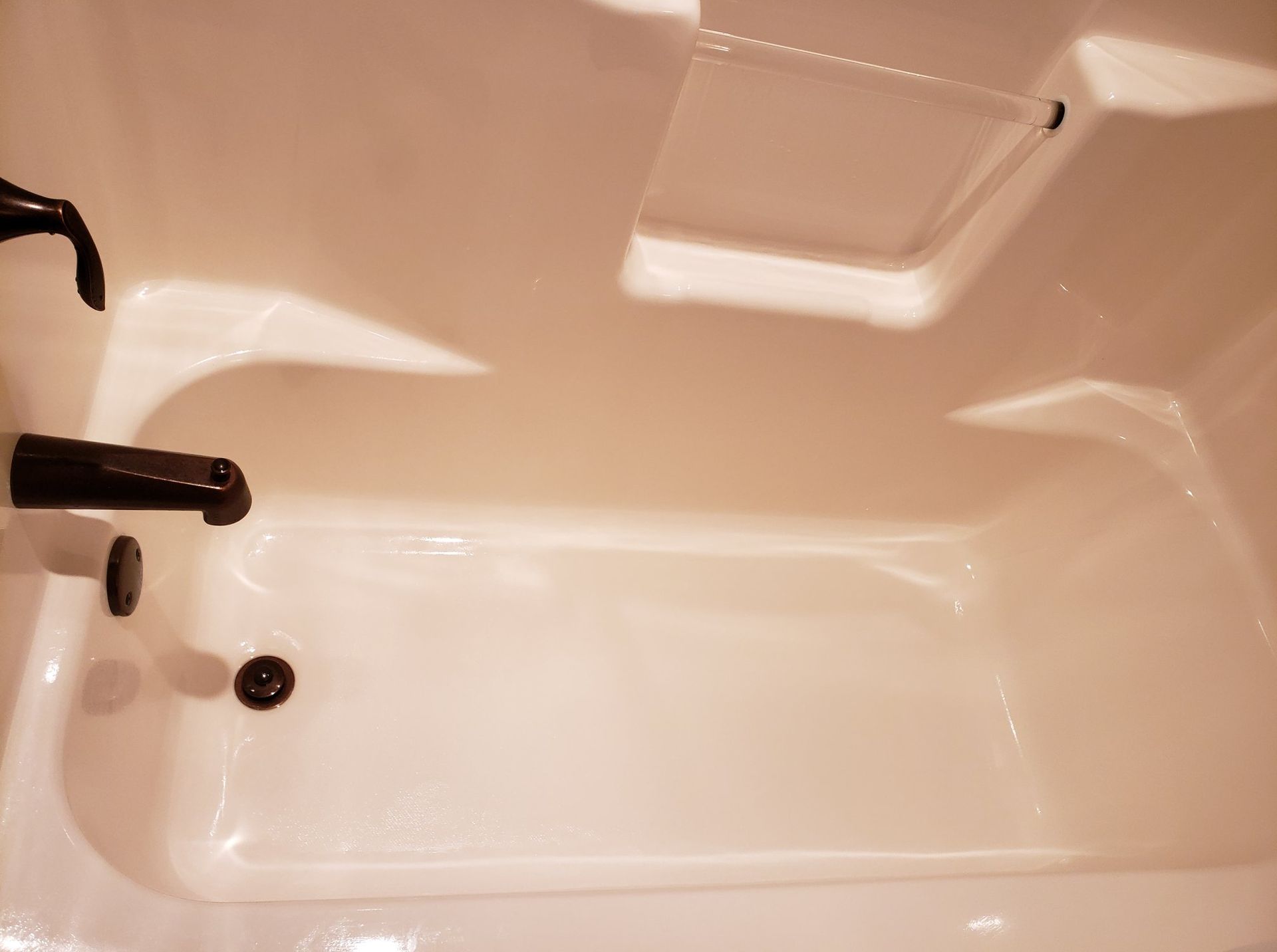 White bathtub with dark fixtures and a clear splash guard.