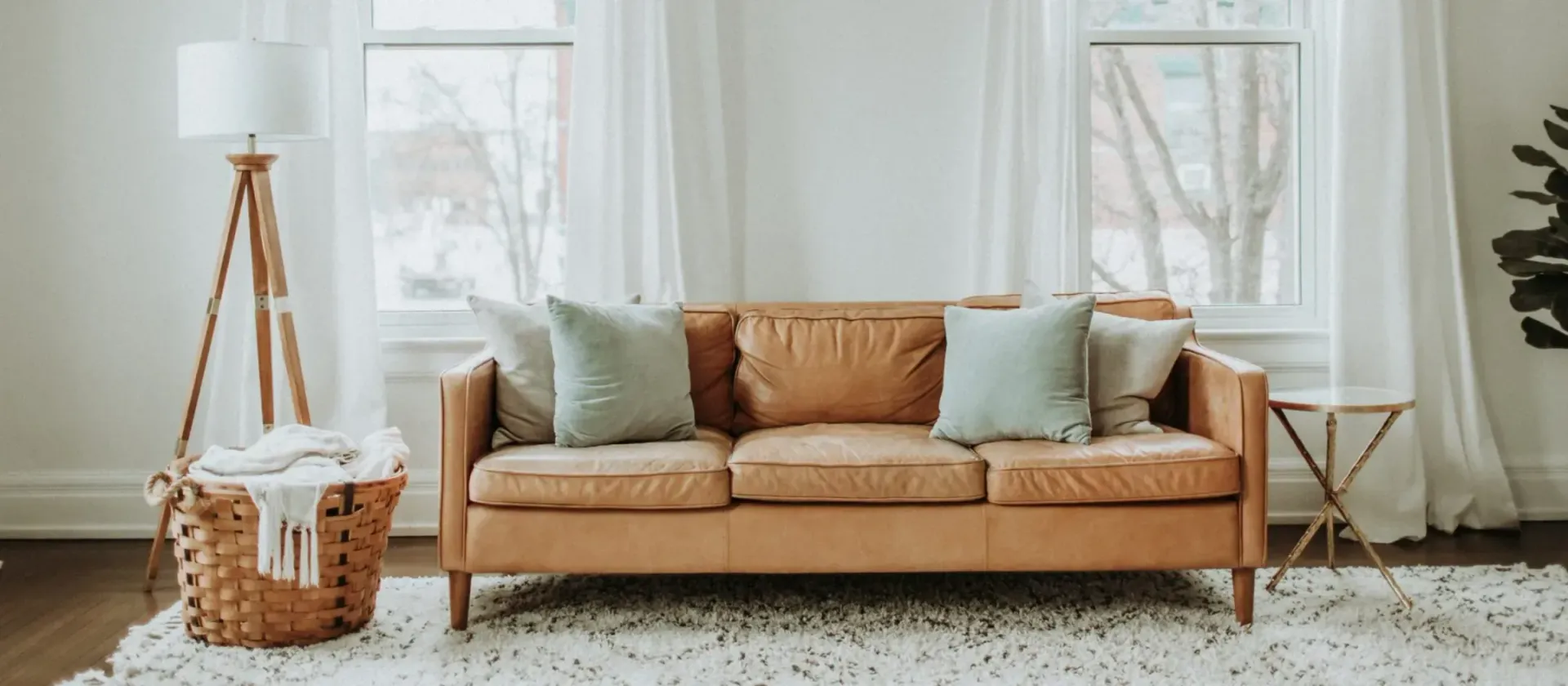 A living room with a leather sofa, pillows, and a basket.