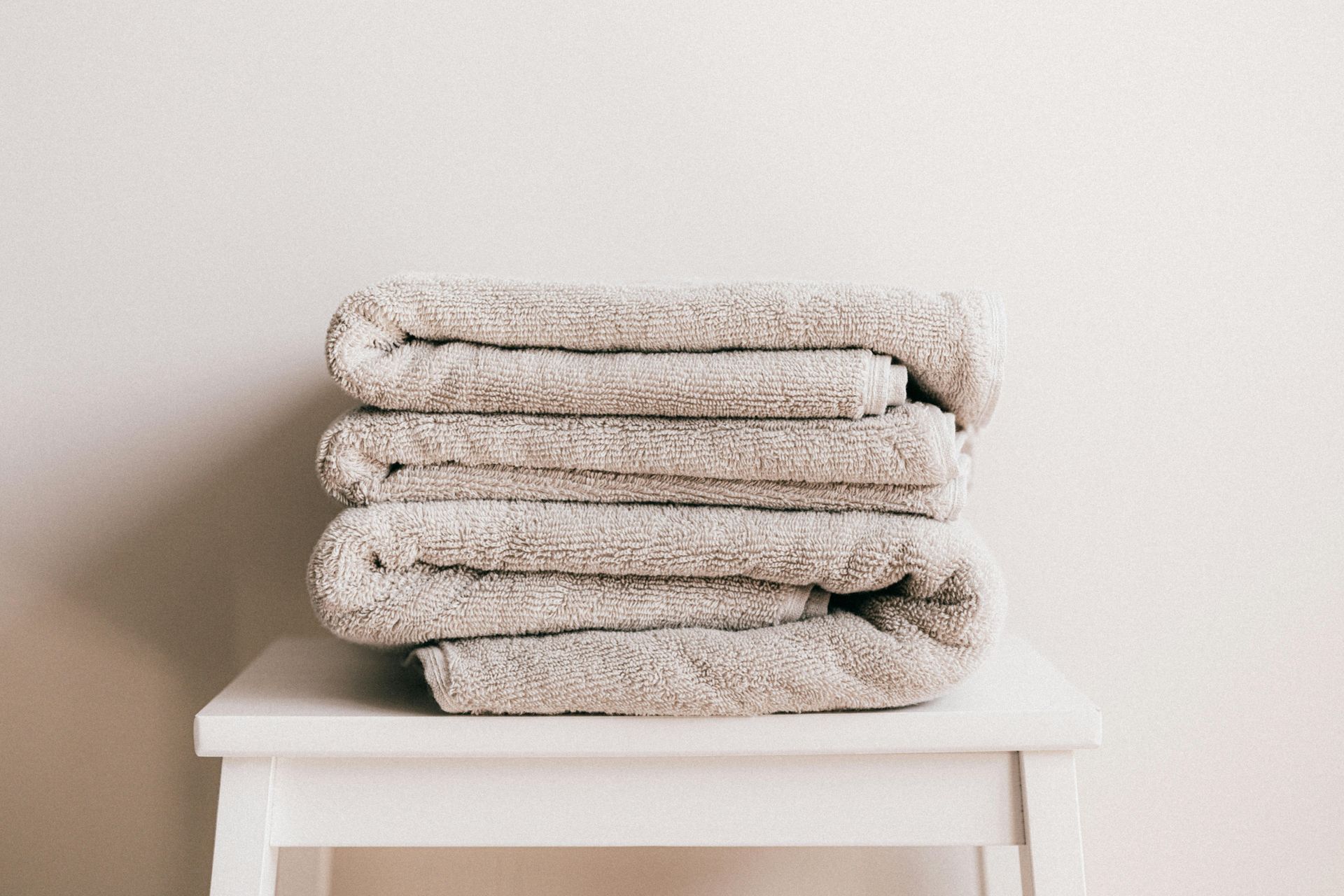 Stack of beige towels on a white stool against a white wall.