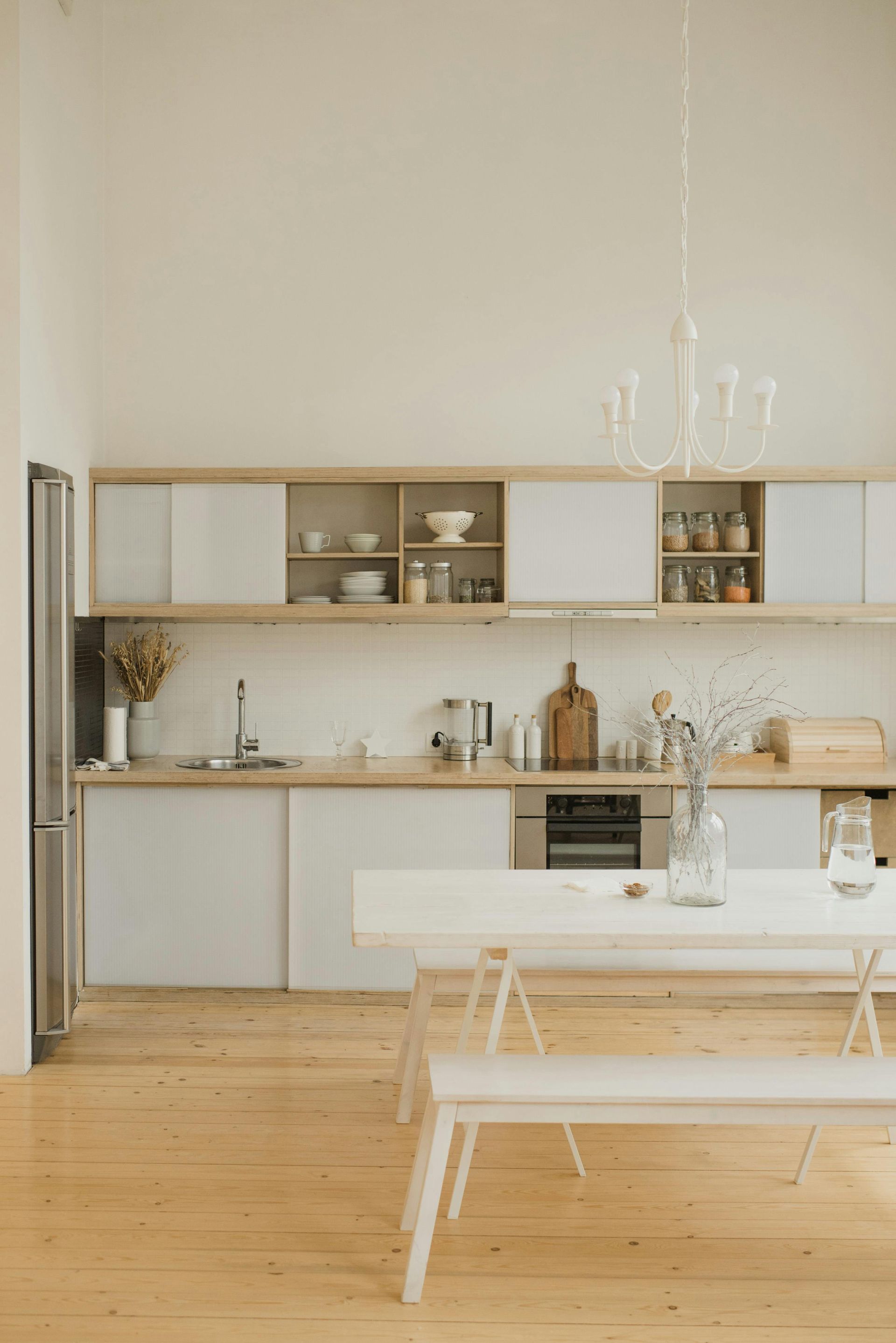 Bright, modern kitchen with white cabinets, wooden floors, and a long white table.
