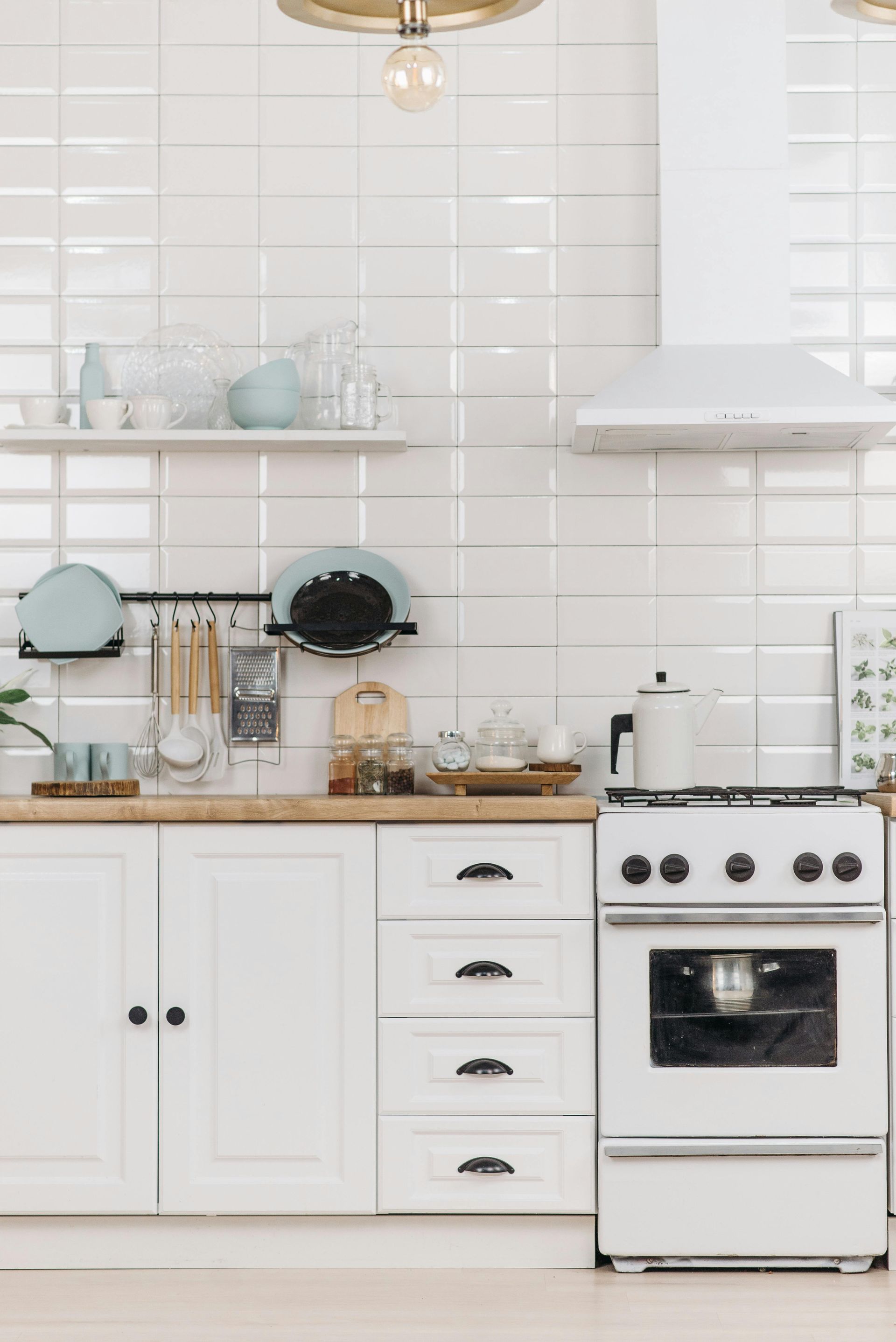 White kitchen with stove, cabinets, and open shelving displaying dishes and cooking utensils.