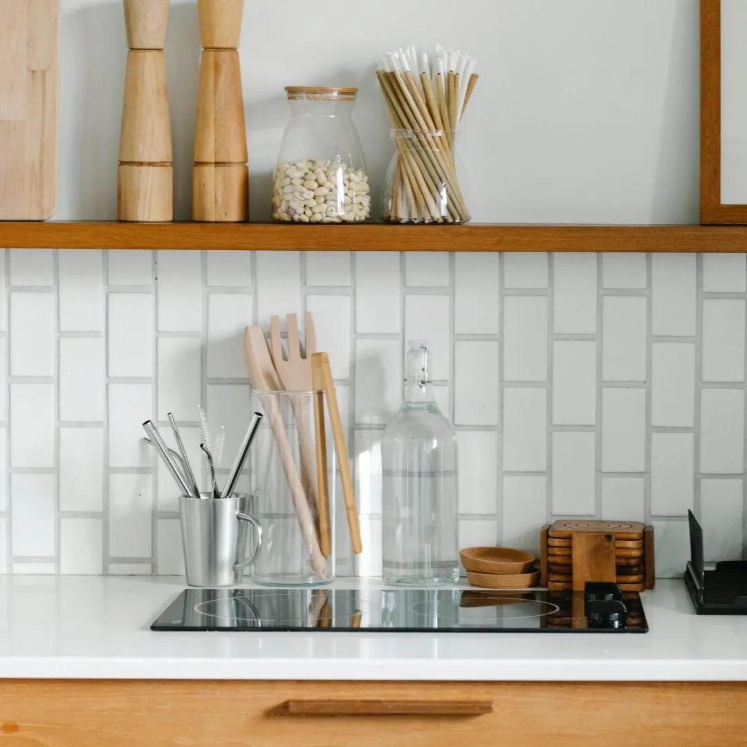 Kitchen countertop with utensils, jars, and shelves of supplies.