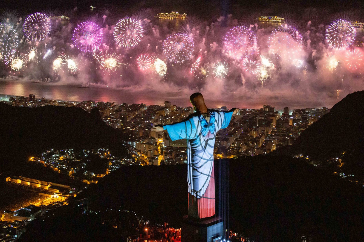 Fogos de artifício explodem sobre o Rio de Janeiro, Brasil. A estátua do Cristo Redentor é iluminada com um desenho colorido.