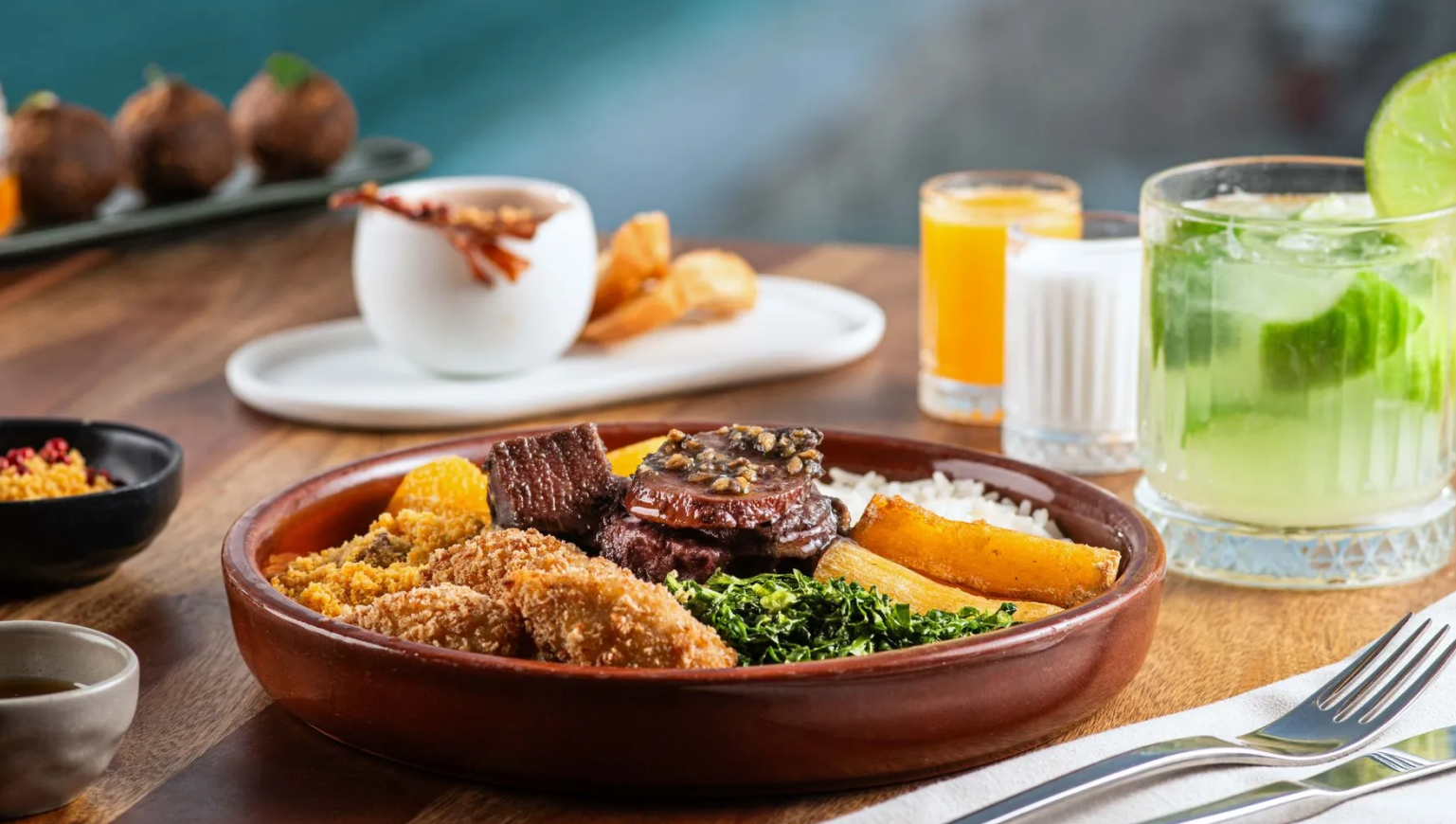 Feijoada brasileira, com arroz, couve e fatias de laranja, servida com bebidas.