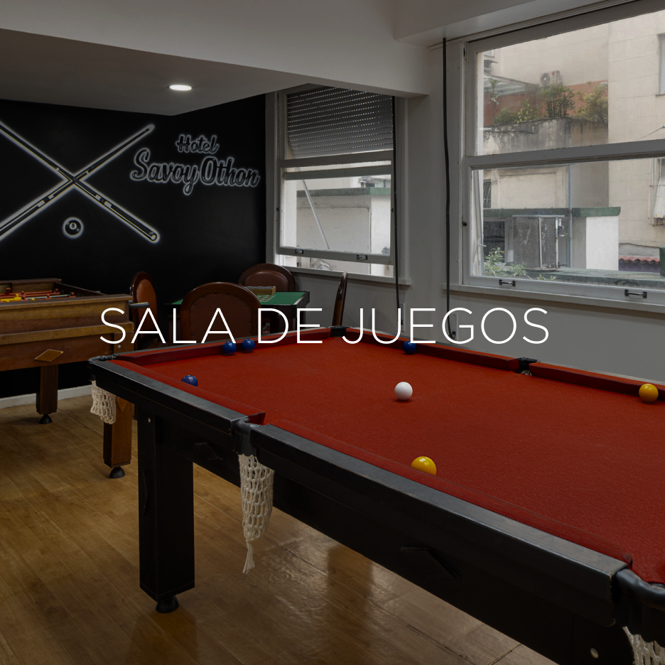 Mesa de bilhar em uma sala de jogos com paredes escuras e janelas. Texto 