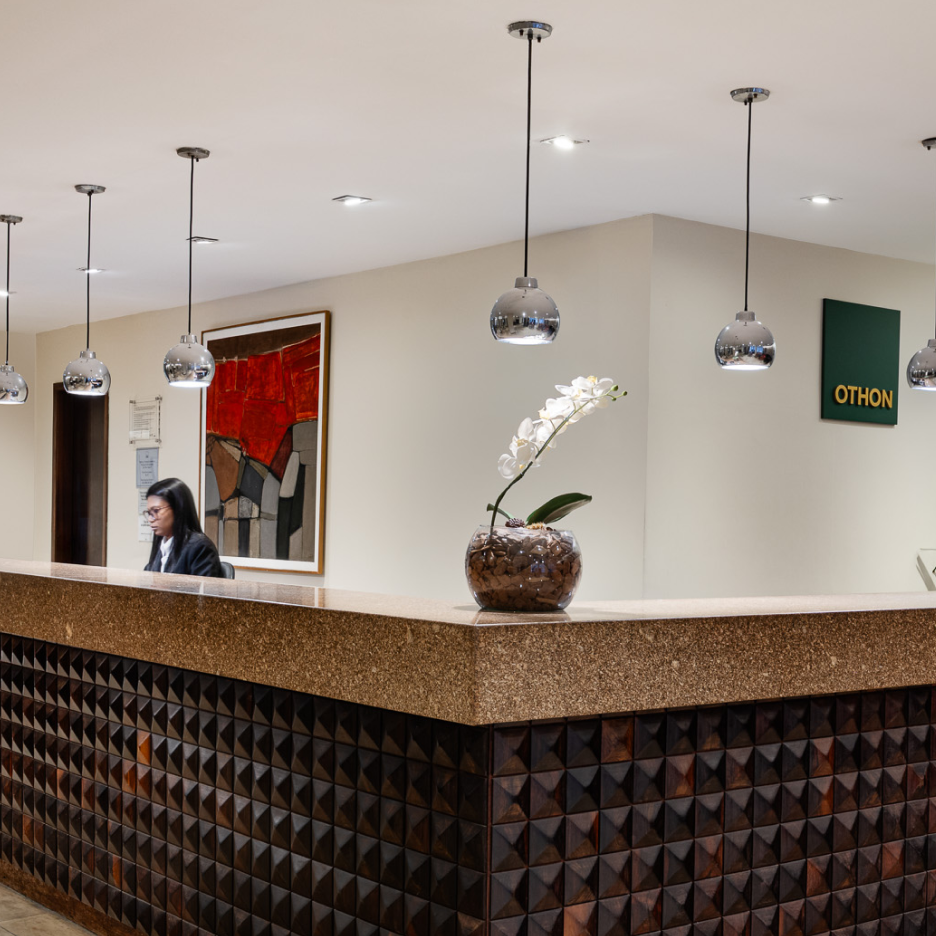 Balcão de recepção com uma pessoa atrás; obras de arte e luzes decorativas.