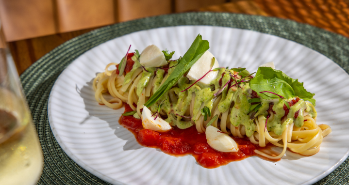Prato de massa com molho verde, tomates, alho e verduras servido em um prato branco.