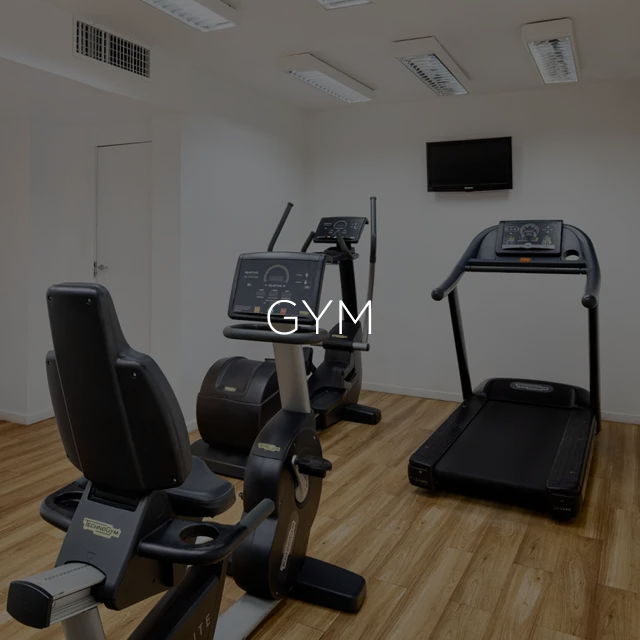 Academia com equipamentos de ginástica: bicicleta ergométrica, elíptico, esteira e TV fixada na parede.