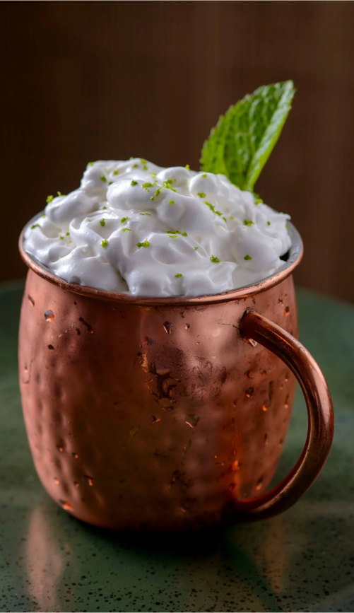 Caneca de cobre cheia de chantilly, decorada com hortelã e raspas de limão.