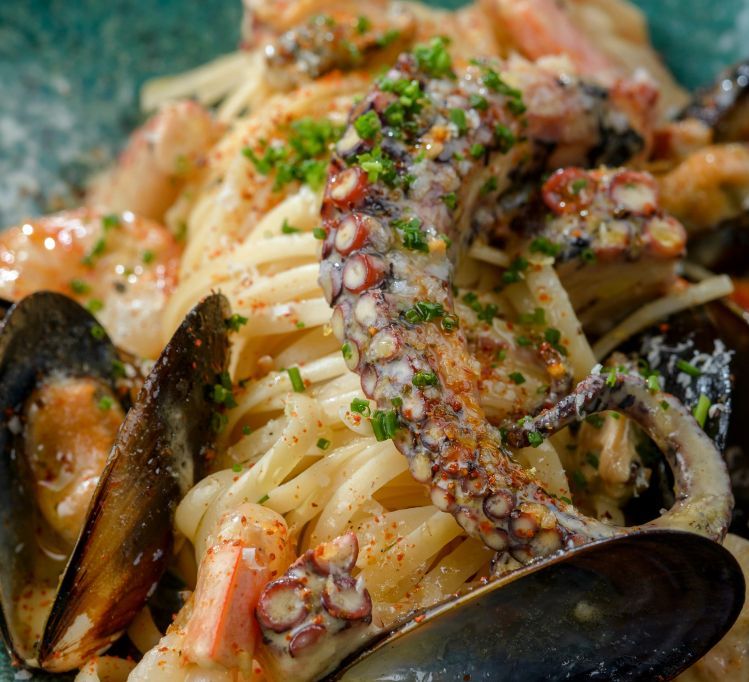 Prato de massa com polvo, mexilhões, camarão e ervas em molho cremoso.