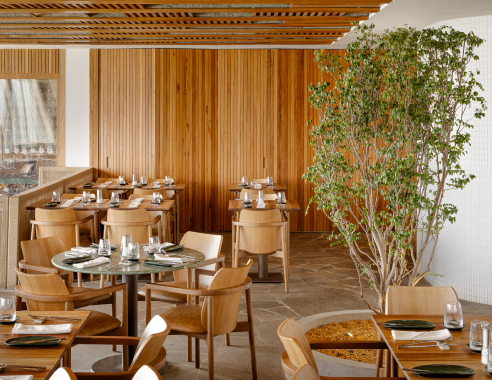 Interior de restaurante com paredes de madeira, mesas, cadeiras e uma pequena árvore.