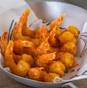 Camarões fritos e bolinhos de milho em uma cesta de metal forrada com papel.