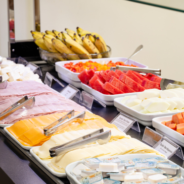 Buffet de café da manhã com frutas fatiadas, queijo, presunto e bananas.