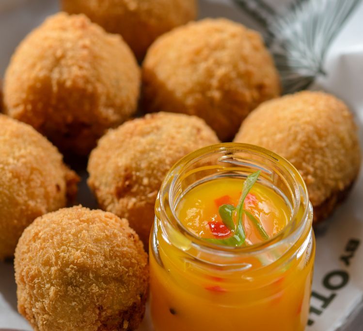 Bolinhos fritos dourados acompanhados de um pequeno frasco de molho amarelo.