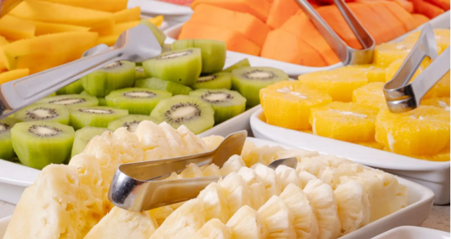 Prato de frutas com abacaxi, kiwi, mamão e manga, servido com pinças.