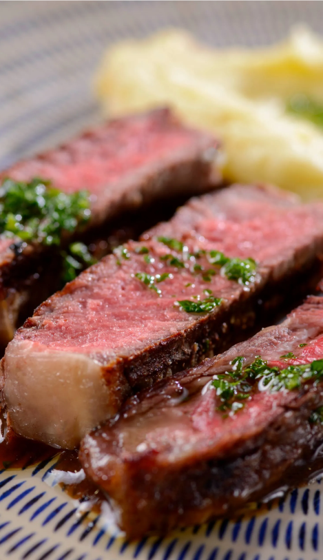 Bife fatiado com guarnição verde e purê de batatas em um prato estampado.