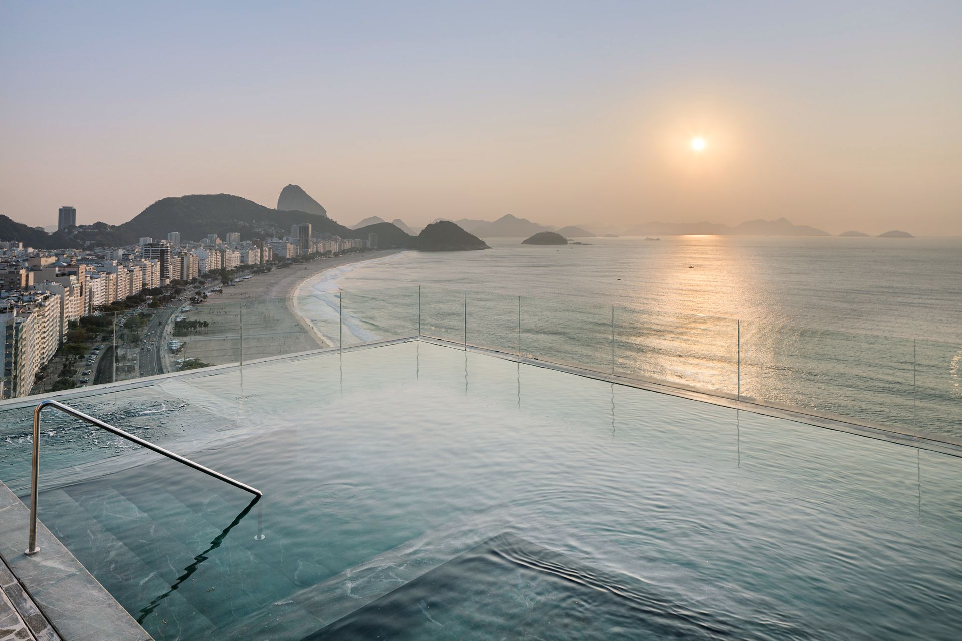 Piscina na cobertura com vista para a praia de Copacabana, no Rio de Janeiro, com o Pão de Açúcar ao fundo, ao pôr do sol.