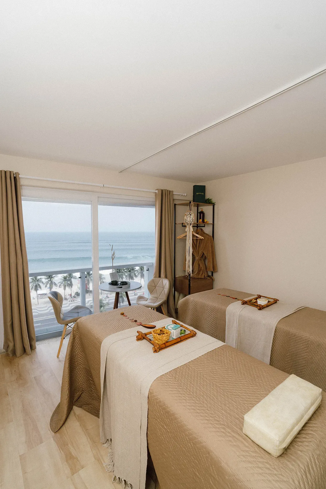 Sala de massagem com vista para o mar; duas mesas de massagem com lençóis brancos e bege.