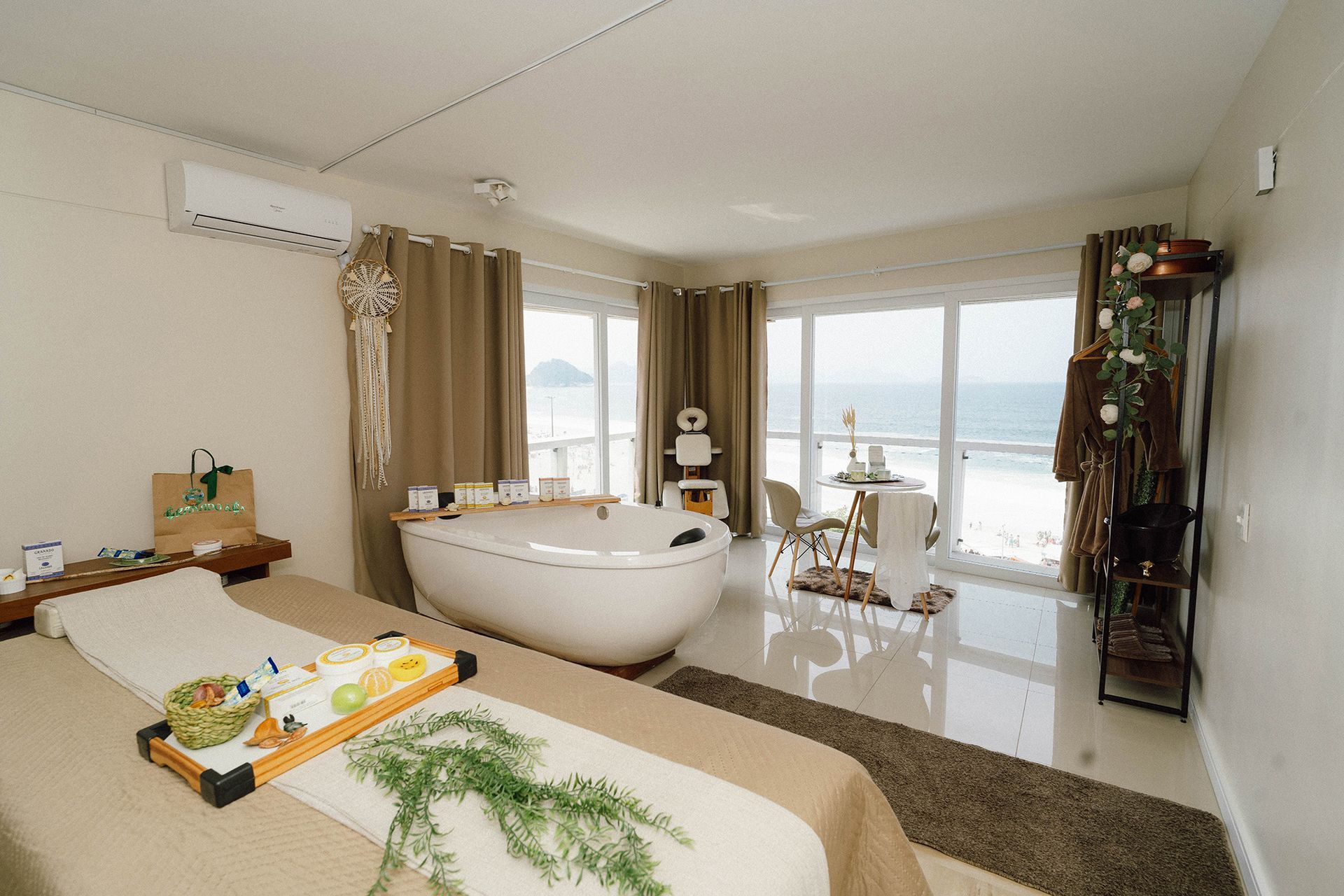Sala de spa com vista para o mar, mesa de massagem, banheira de imersão e itens decorativos.