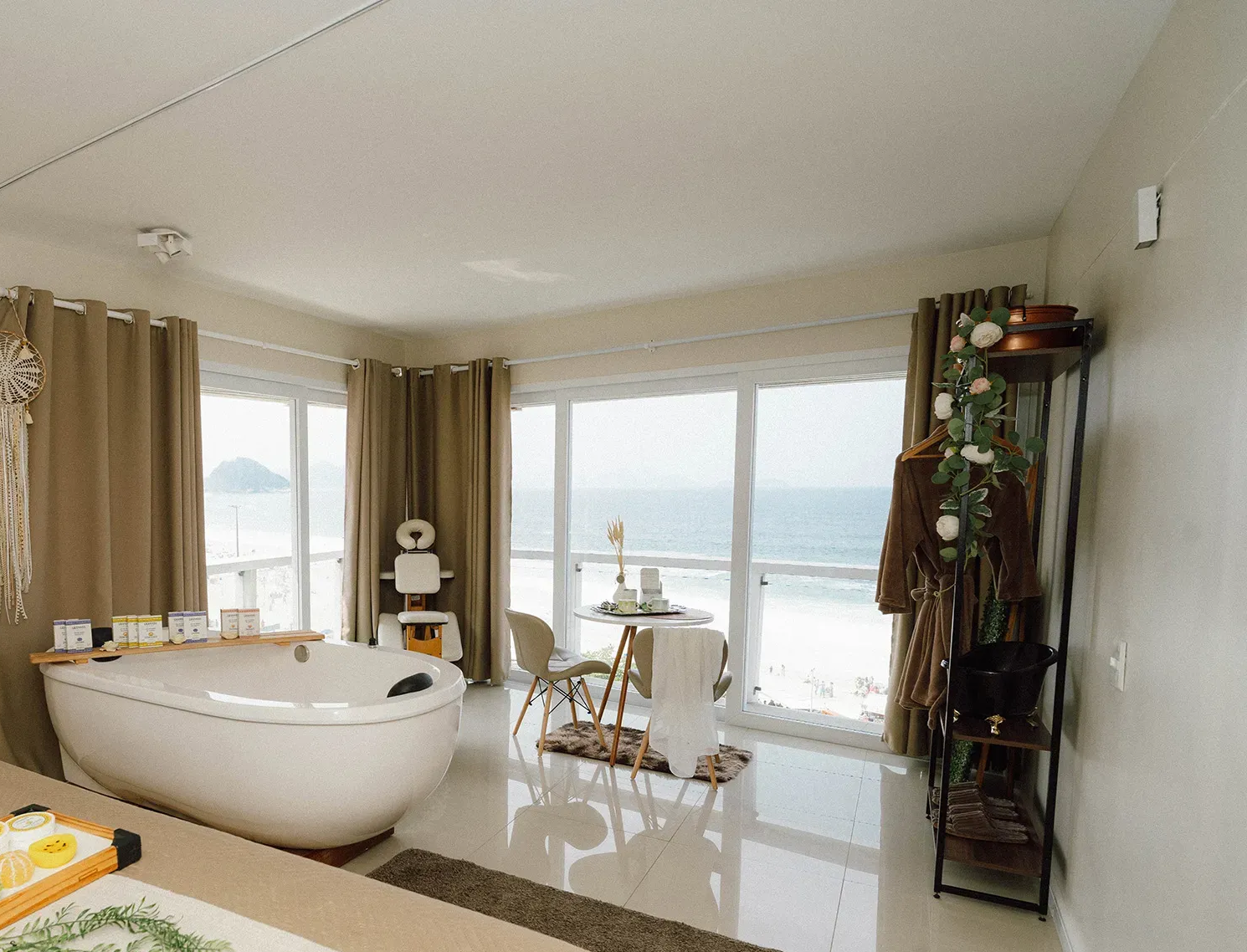 Banheiro com banheira grande, vista para o mar e uma pequena mesa com cadeiras.
