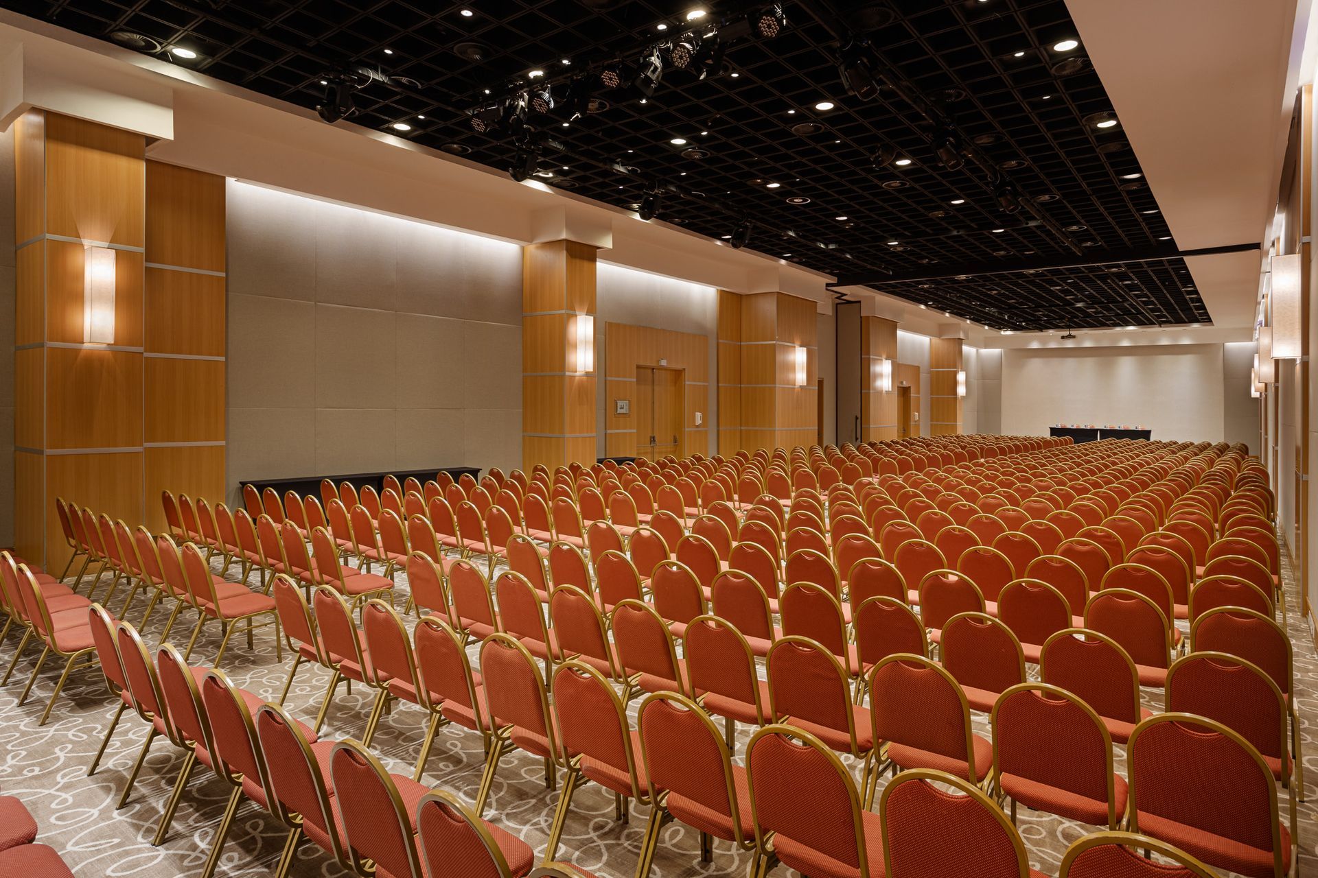 Auditório vazio com fileiras de cadeiras vermelhas, painéis de madeira e teto preto.