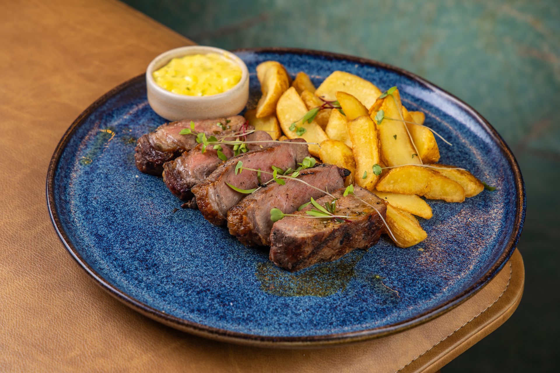 Bife fatiado, batatas em gomos e molho num prato azul.