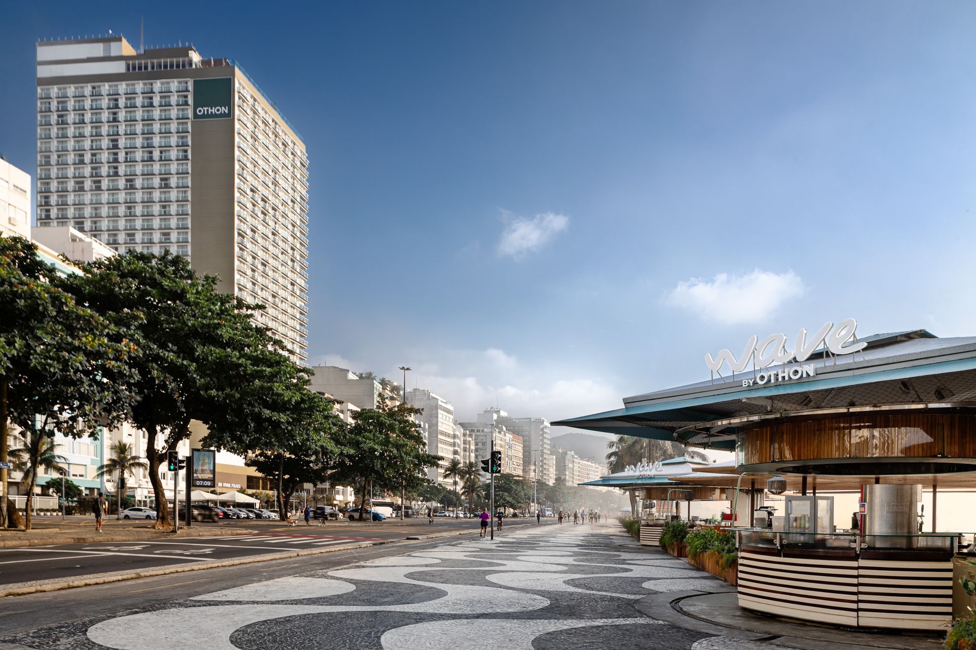 Calçadão da Praia de Copacabana, Rio de Janeiro. Calçada com mosaico em preto e branco, prédios, árvores, céu limpo.