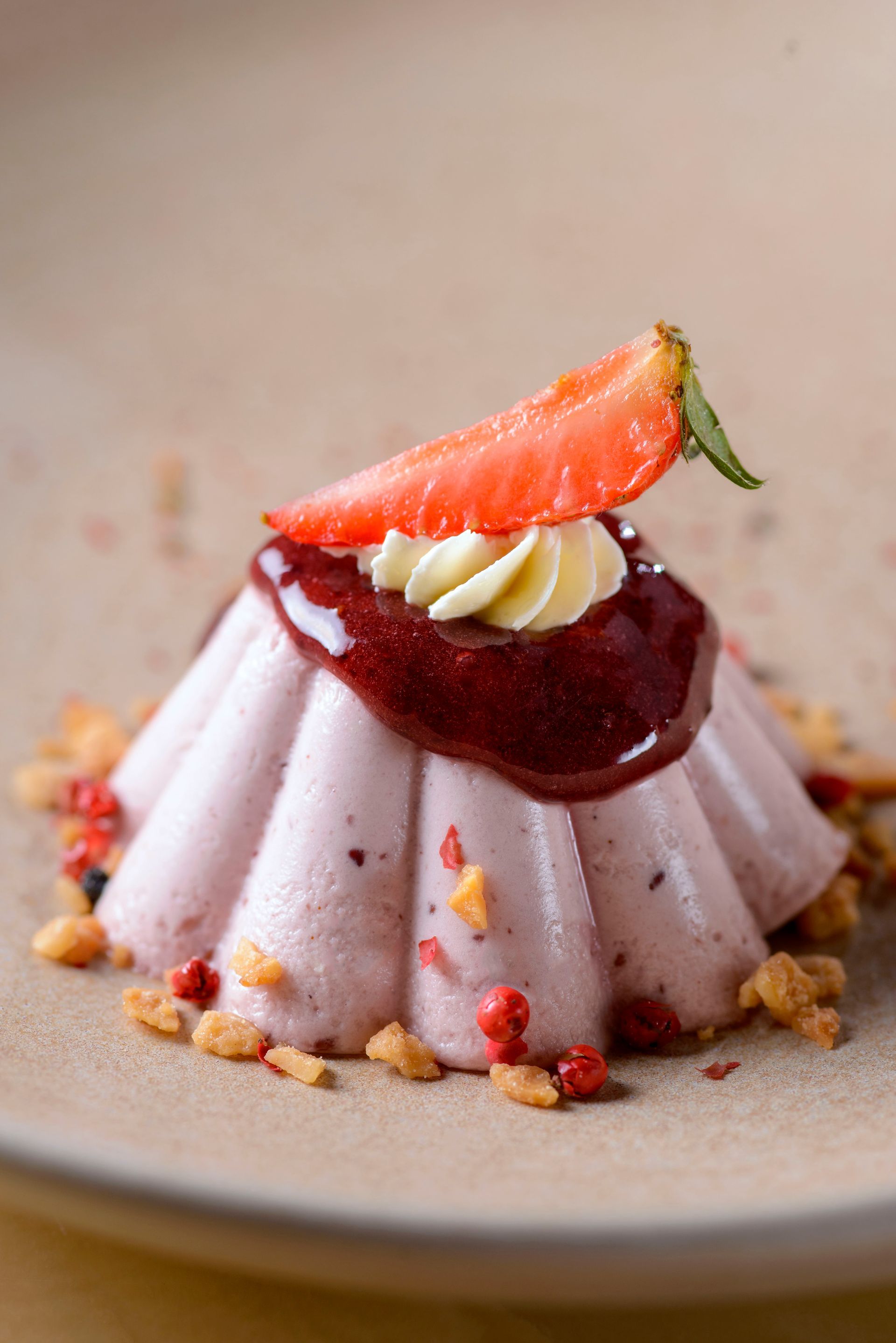 Sobremesa de panna cotta de morango com calda e decoração em um prato bege.
