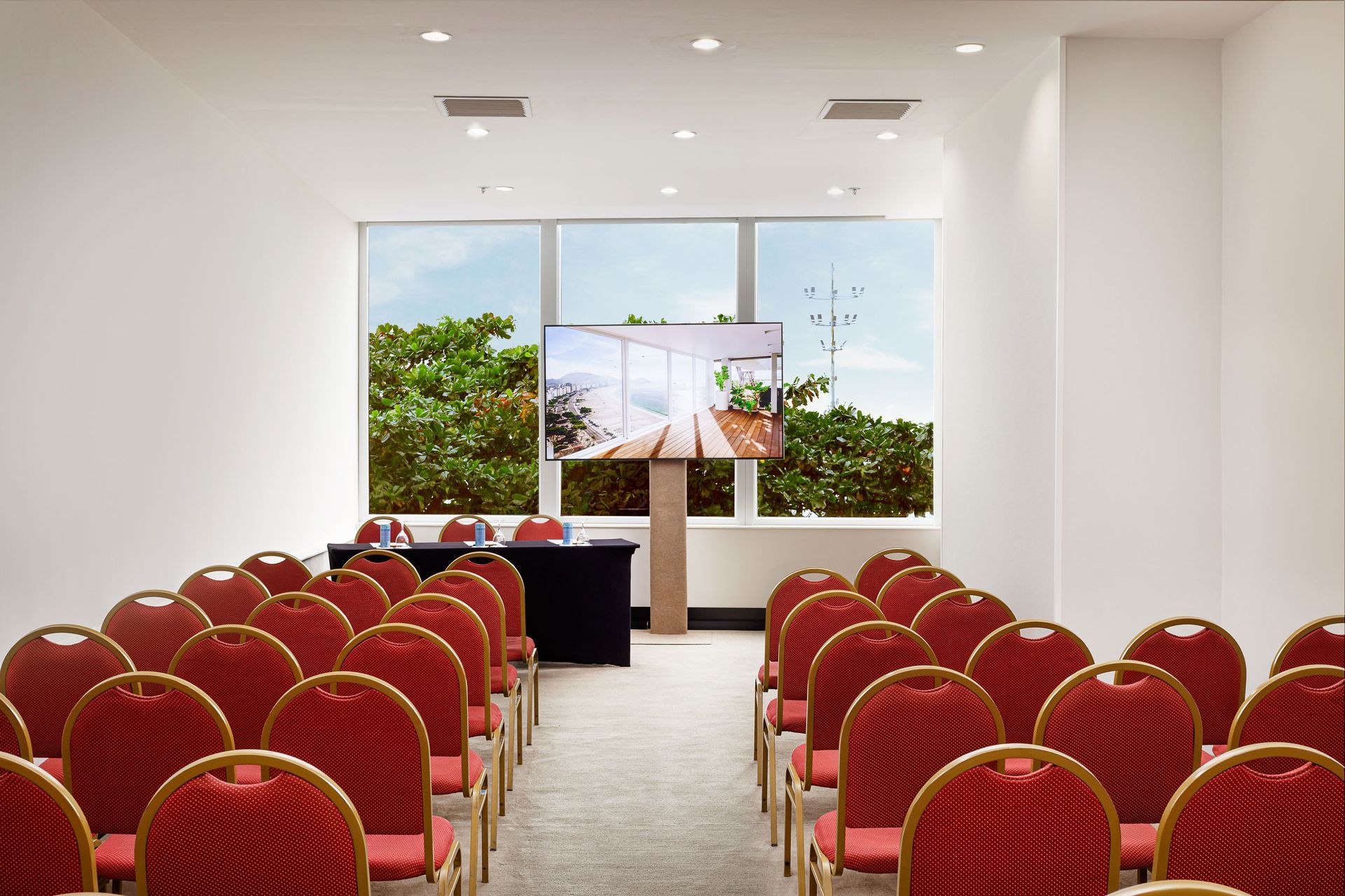 Uma sala de conferências com cadeiras vermelhas e uma grande TV de tela plana.