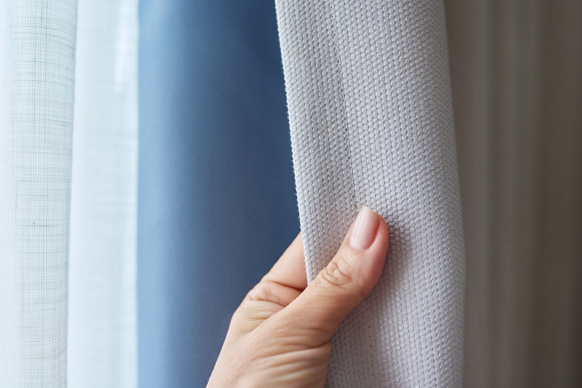 A close-up of a hand touching different types and colours of curtain fabric.