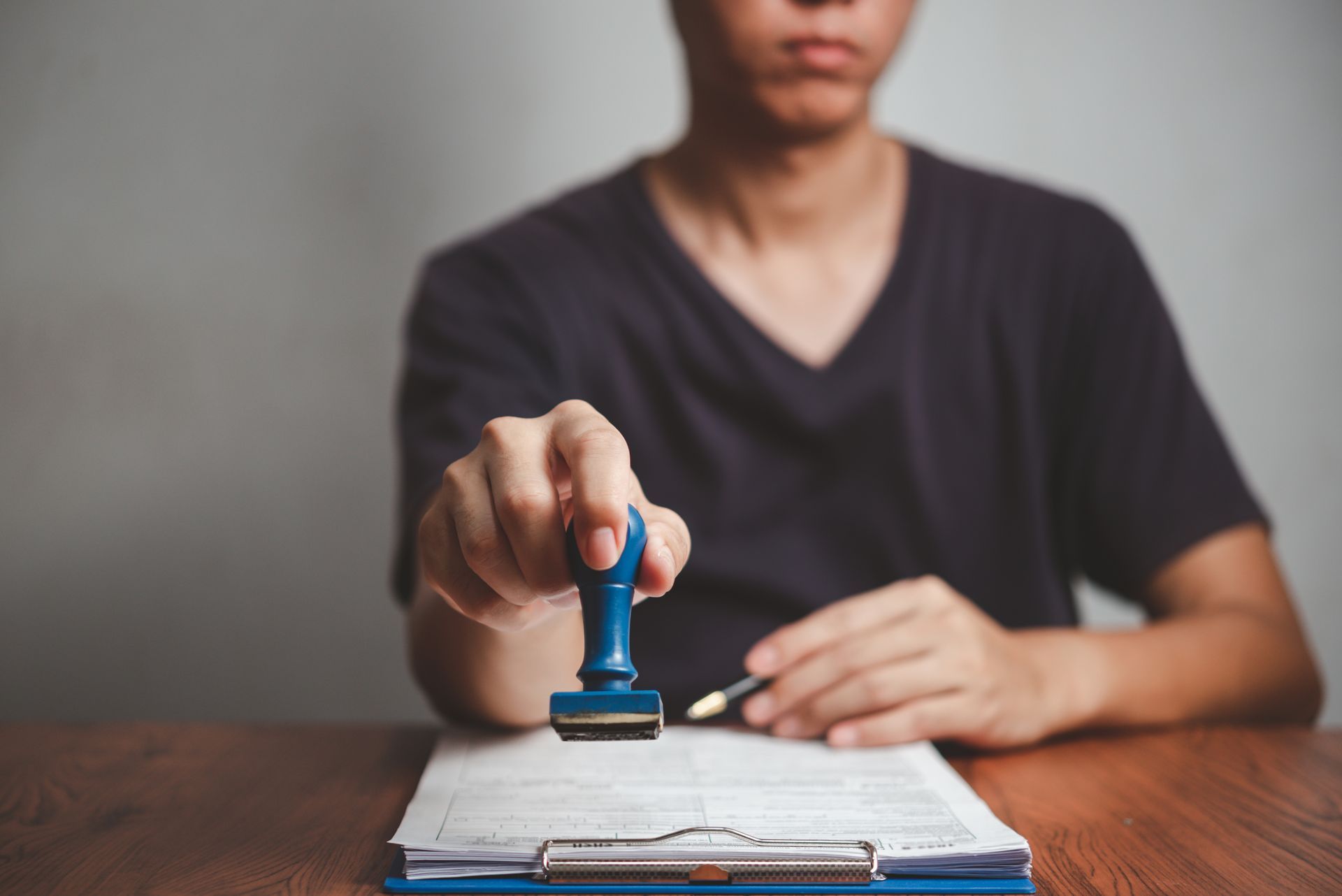 Person holding a blue stamp over a clipboard with a document, ready to stamp.