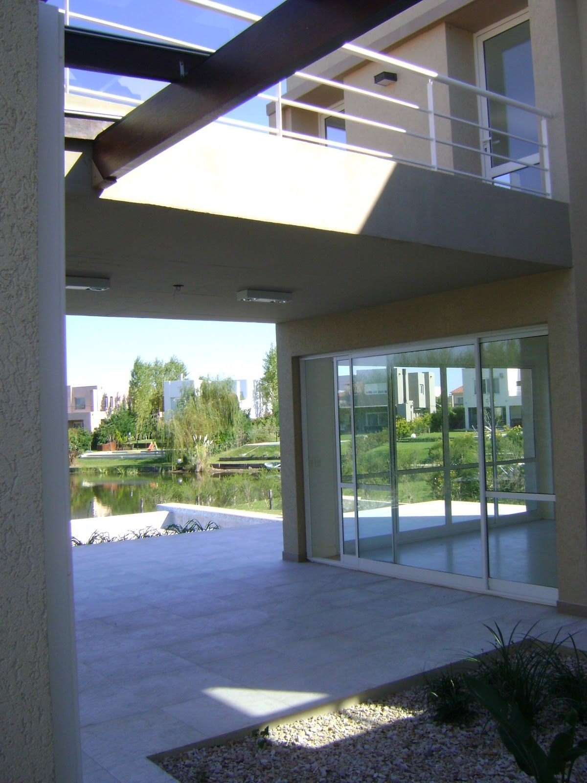 Un patio cubierto con suelo de piedra clara con vistas a una zona de césped y un pequeño lago, con un edificio encima.