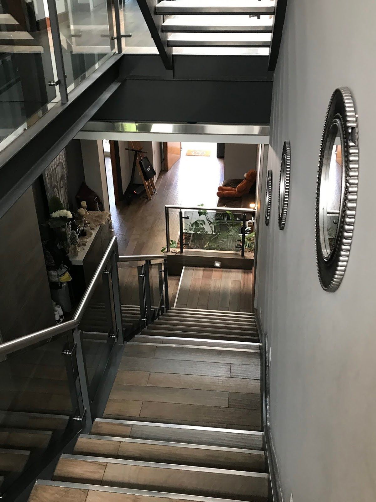 Vista desde una escalera de madera con barandillas de cristal y detalles metálicos que da a un pasillo diáfano con espejos 