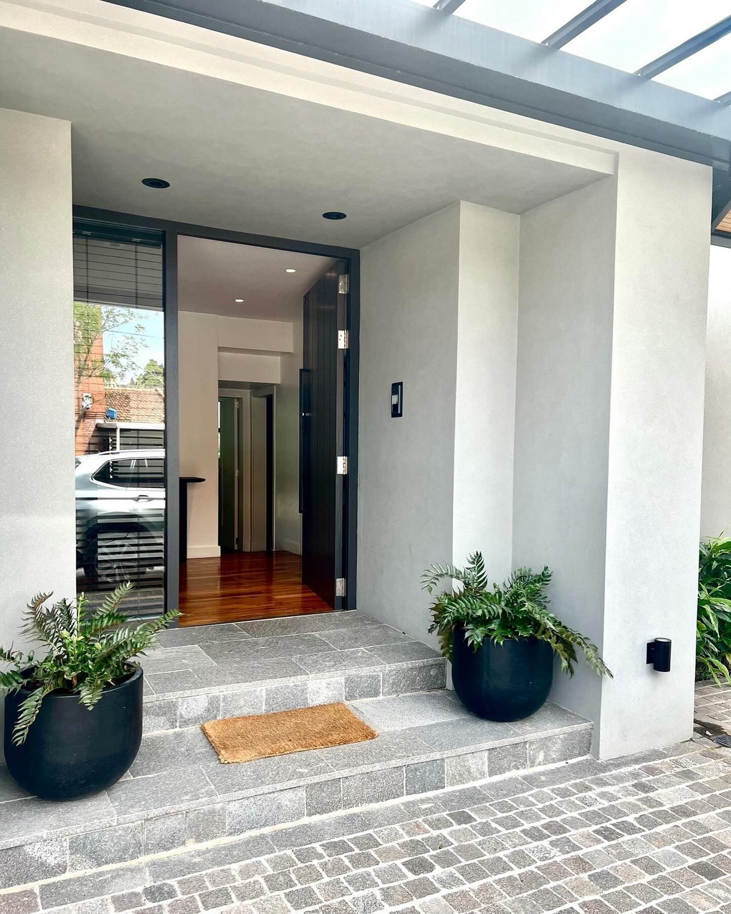 Entrada principal de una casa con paredes blancas, escalones de piedra gris