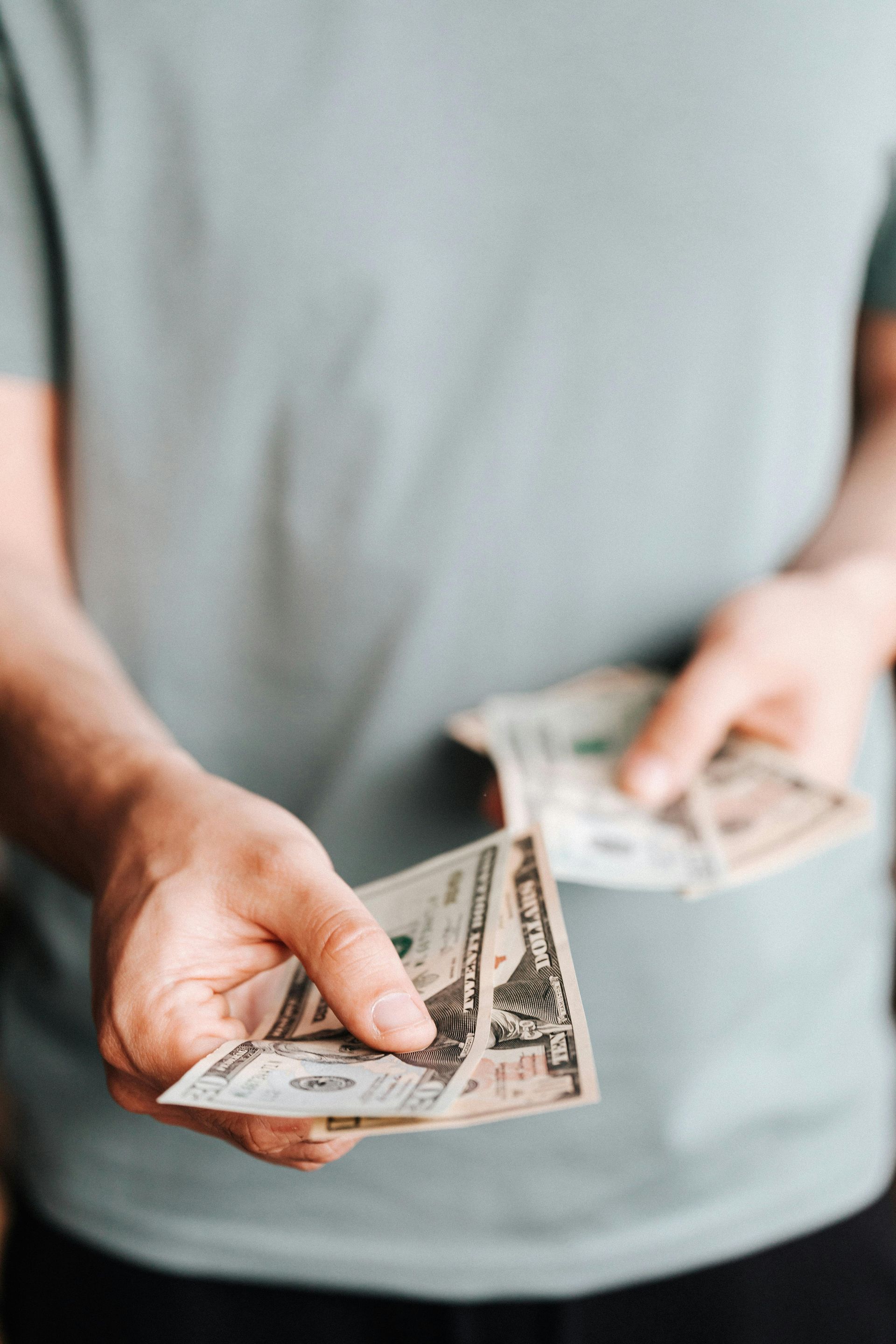 A person in a light blue t-shirt holds out US paper currency in their hands.