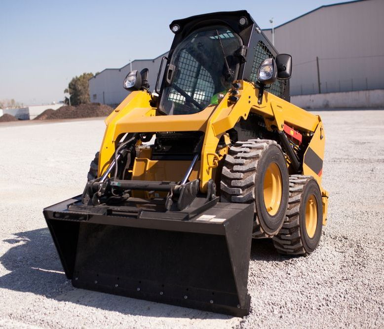 A Yellow Tractor With a Black Bucket is Parked in a Gravel Lot — One Group Industries Pty Ltd in Bathurst, NSW
